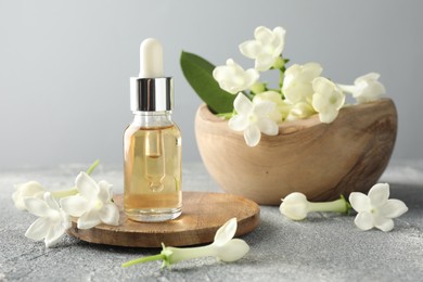 Photo of Bottle of essential oil and jasmine flowers on grey table