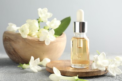 Photo of Bottle of essential oil and jasmine flowers on grey table, closeup