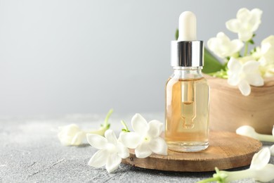 Photo of Bottle of essential oil and jasmine flowers on grey table, closeup. Space for text