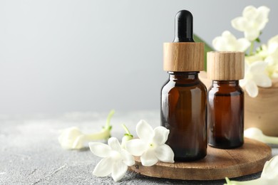 Photo of Bottles of essential oil and jasmine flowers on grey table, closeup. Space for text
