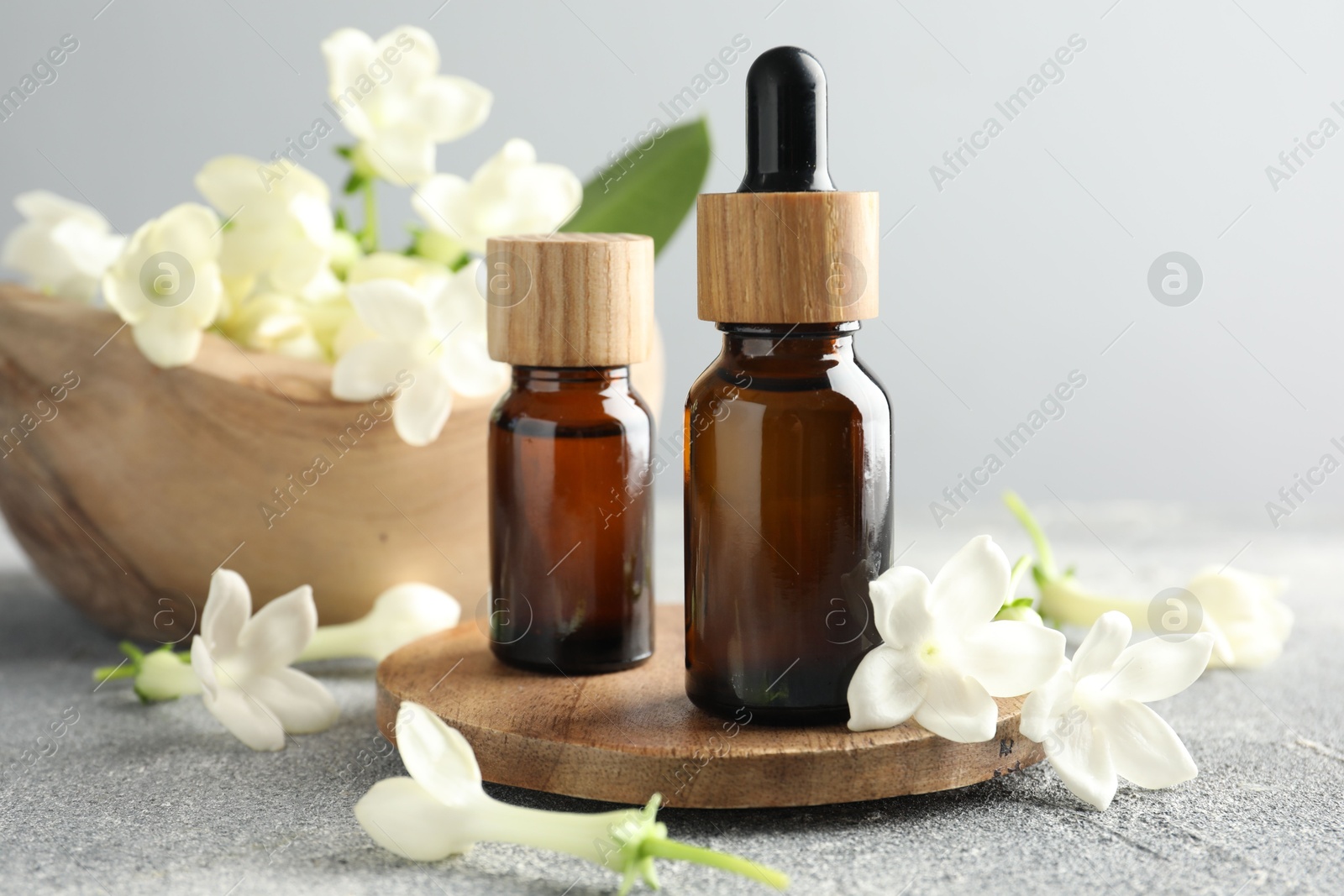 Bottles of essential oil and jasmine flowers on grey table, closeup Photo of Bottles of essential oil and jasmine flowers on grey table, closeup