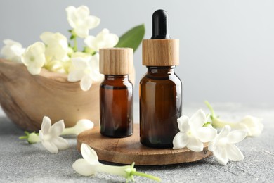 Photo of Bottles of essential oil and jasmine flowers on grey table, closeup