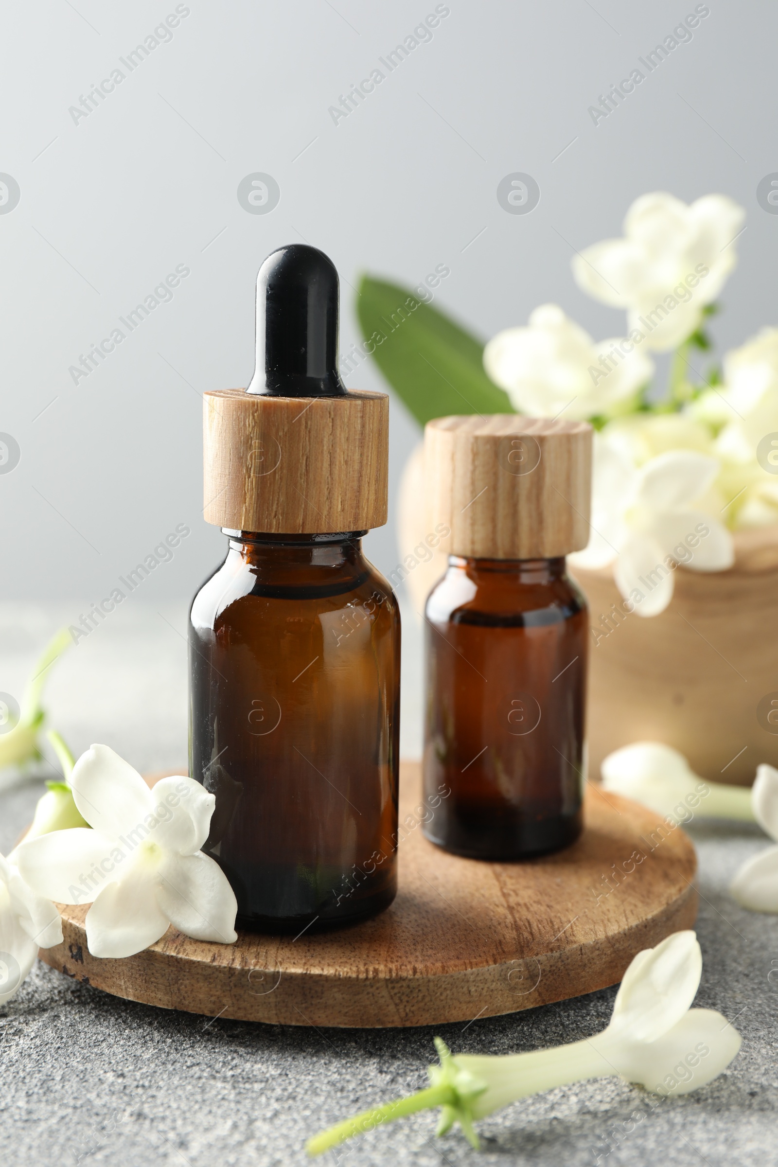 Bottles of essential oil and jasmine flowers on grey table, closeup Photo of Bottles of essential oil and jasmine flowers on grey table, closeup