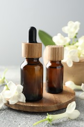 Photo of Bottles of essential oil and jasmine flowers on grey table, closeup