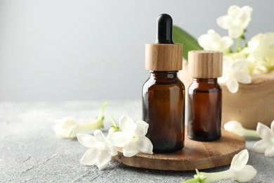 Photo of Bottles of essential oil and jasmine flowers on grey table, closeup. Space for text