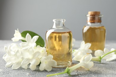Photo of Bottles of essential oil and jasmine flowers on grey table, closeup