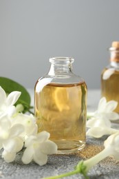 Photo of Bottles of essential oil and jasmine flowers on grey table, closeup
