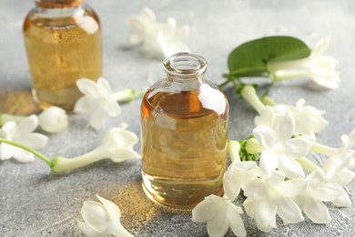 Photo of Bottles of essential oil and jasmine flowers on grey table, closeup