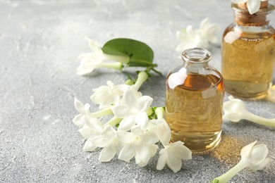 Photo of Bottles of essential oil and jasmine flowers on grey table, closeup. Space for text