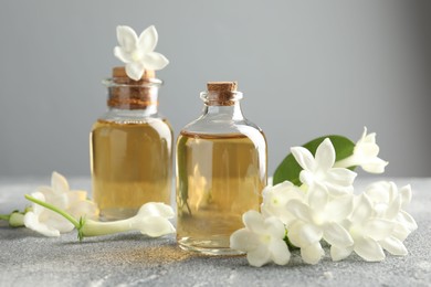 Photo of Bottles of essential oil and jasmine flowers on grey table, closeup