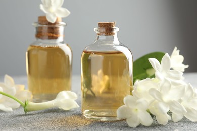Photo of Bottles of essential oil and jasmine flowers on grey table, closeup
