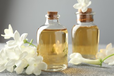 Photo of Bottles of essential oil and jasmine flowers on grey table, closeup