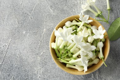 Photo of Beautiful jasmine flowers in bowl on grey table, flat lay. Space for text