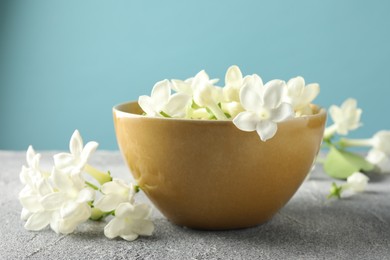Photo of Beautiful jasmine flowers in bowl on grey table against light blue background, closeup