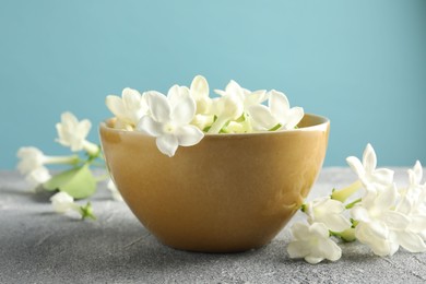 Photo of Beautiful jasmine flowers in bowl on grey table against light blue background, closeup