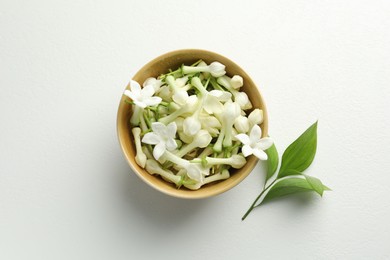 Photo of Beautiful jasmine flowers in bowl and green leaves on white table, flat lay