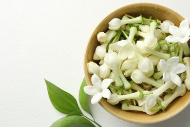 Photo of Beautiful jasmine flowers in bowl and green leaves on white table, flat lay. Space for text