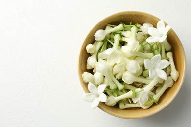 Photo of Beautiful jasmine flowers in bowl on white table, top view. Space for text