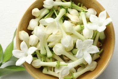 Photo of Beautiful jasmine flowers in bowl and green leaves on white table, flat lay