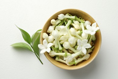Photo of Beautiful jasmine flowers in bowl and green leaves on white table, flat lay