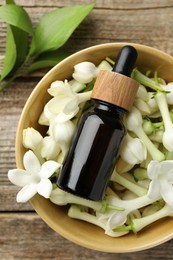 Photo of Bottle of essential oil and jasmine flowers in bowl on wooden table, flat lay
