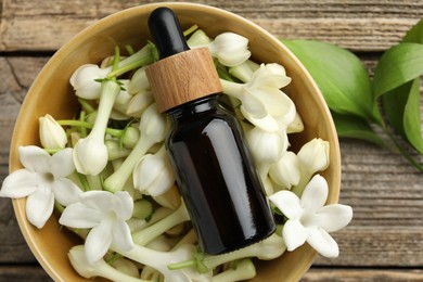 Photo of Bottle of essential oil and jasmine flowers in bowl on wooden table, flat lay