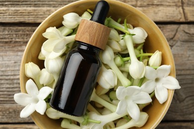Photo of Bottle of essential oil and jasmine flowers in bowl on wooden table, top view