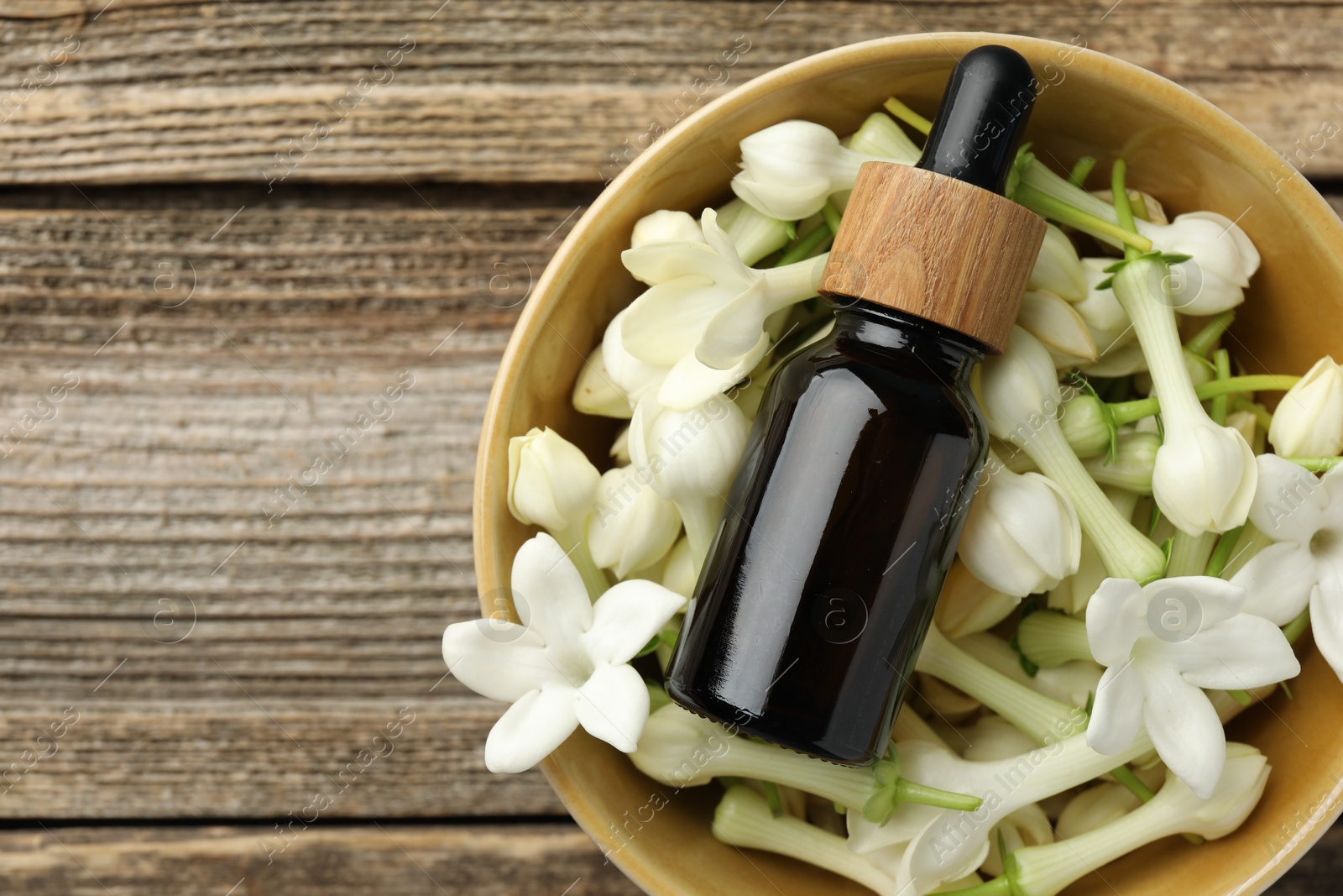 Bottle of essential oil and jasmine flowers in bowl on wooden table, top view. Space for text Photo of Bottle of essential oil and jasmine flowers in bowl on wooden table, top view. Space for text