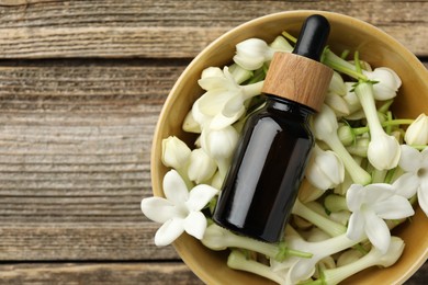 Photo of Bottle of essential oil and jasmine flowers in bowl on wooden table, top view. Space for text