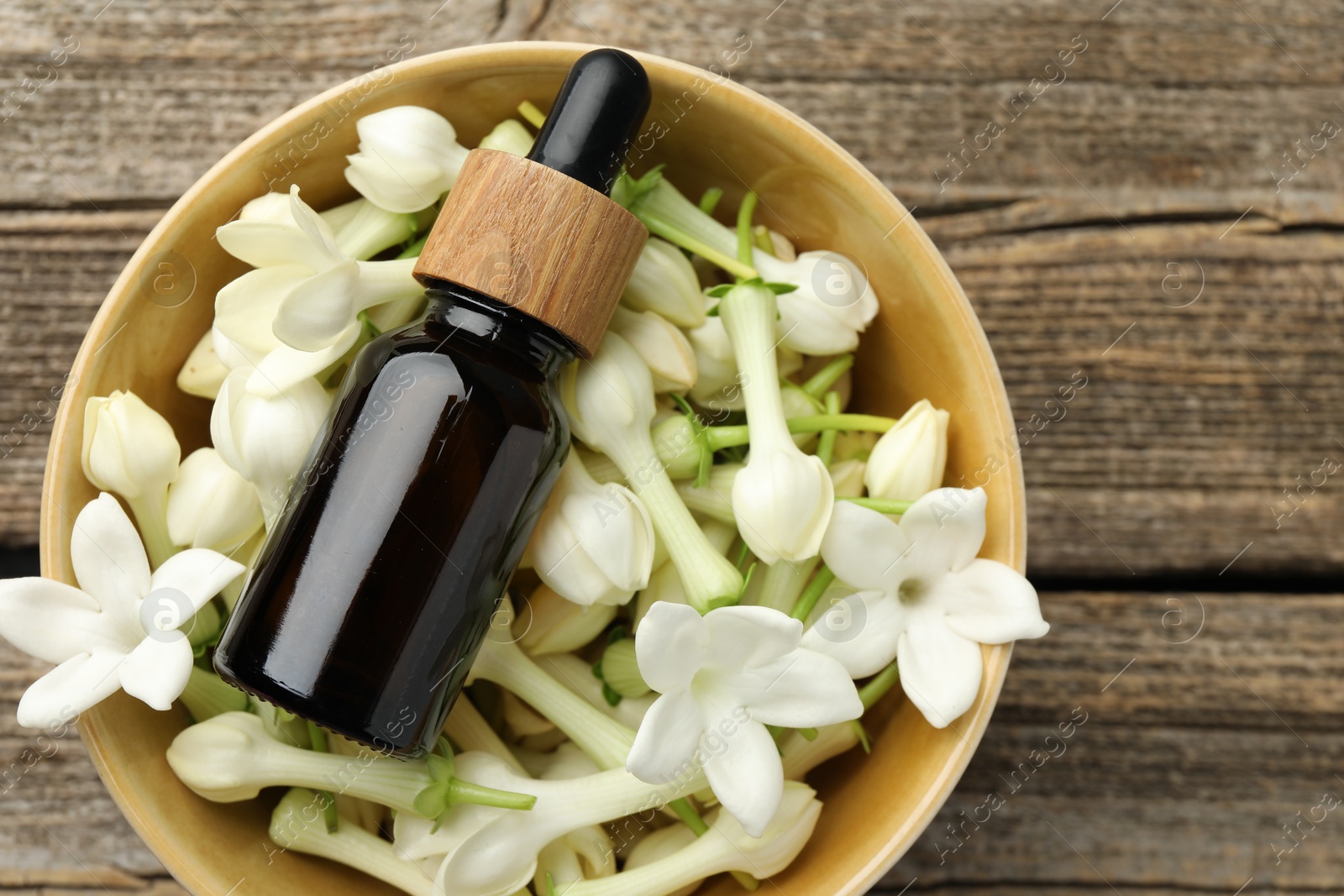 Bottle of essential oil and jasmine flowers in bowl on wooden table, top view Photo of Bottle of essential oil and jasmine flowers in bowl on wooden table, top view