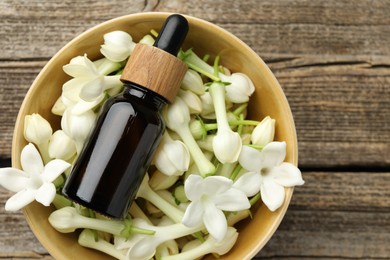 Photo of Bottle of essential oil and jasmine flowers in bowl on wooden table, top view