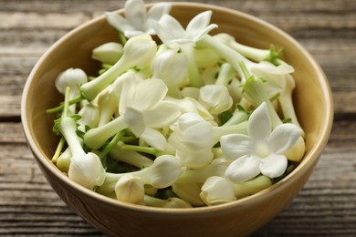 Photo of Beautiful jasmine flowers in bowl on wooden table, closeup