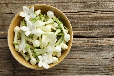 Photo of Beautiful jasmine flowers in bowl on wooden table, top view. Space for text