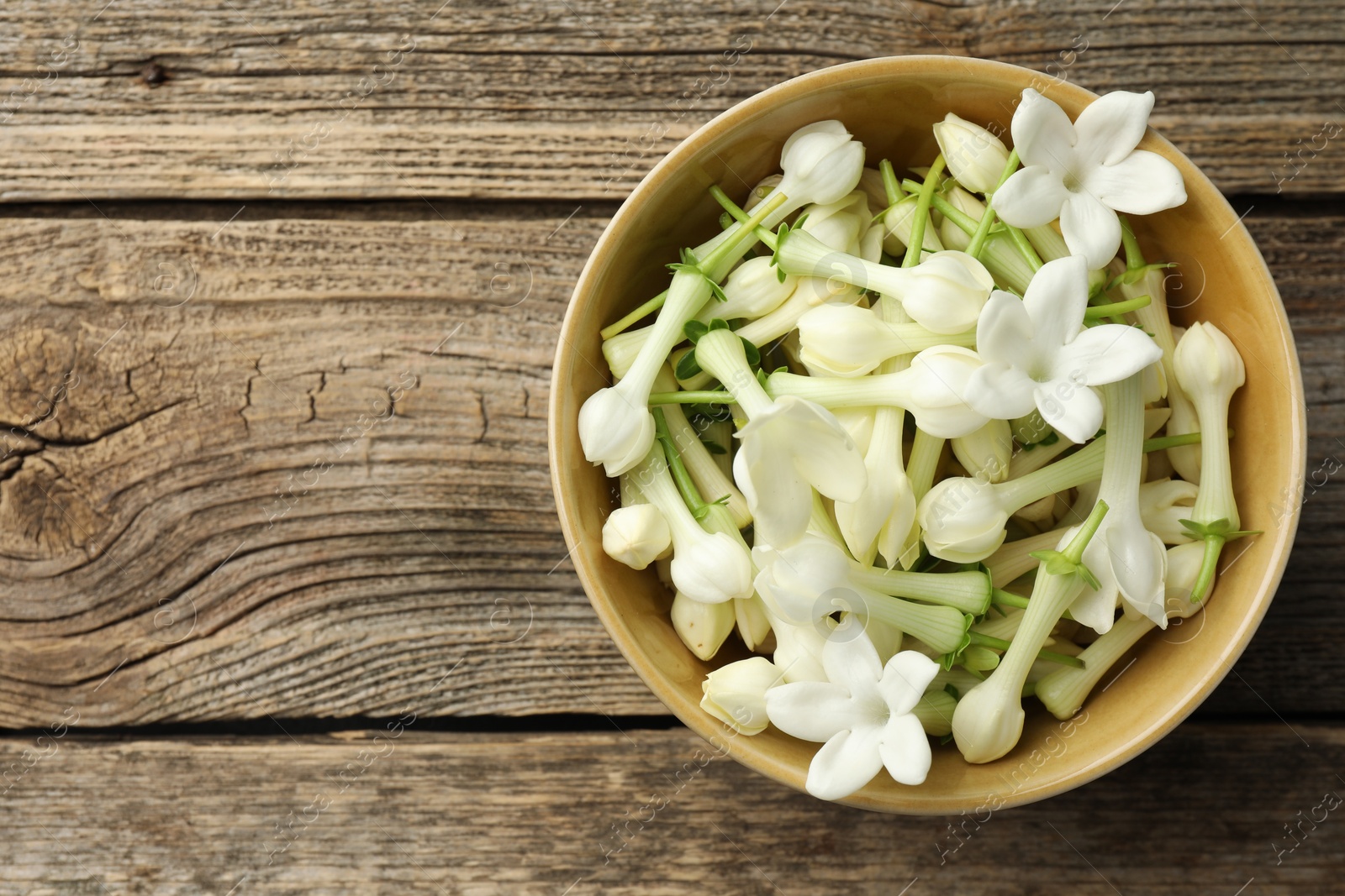 Beautiful jasmine flowers in bowl on wooden table, top view. Space for text Photo of Beautiful jasmine flowers in bowl on wooden table, top view. Space for text