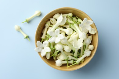 Photo of Beautiful jasmine flowers in bowl on light blue background, top view
