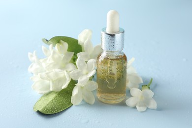 Photo of Bottle of essential oil, jasmine flowers and green leaves on light blue background, closeup