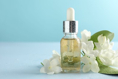 Photo of Bottle of essential oil, jasmine flowers and green leaves on light blue background, closeup. Space for text