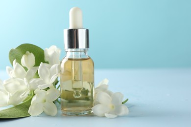 Photo of Bottle of essential oil, jasmine flowers and green leaves on light blue background, closeup. Space for text