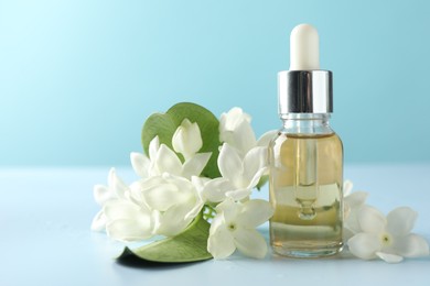 Photo of Bottle of essential oil, jasmine flowers and green leaves on light blue background, closeup