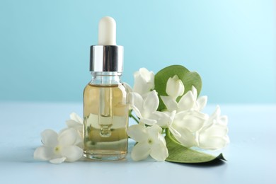 Photo of Bottle of essential oil, jasmine flowers and green leaves on light blue background, closeup