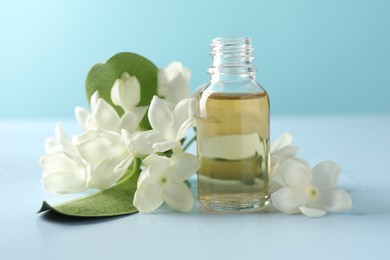 Photo of Bottle of essential oil, jasmine flowers and green leaves on light blue background, closeup