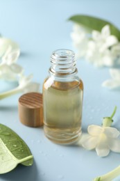 Photo of Bottle of essential oil and jasmine flowers on light blue background, closeup