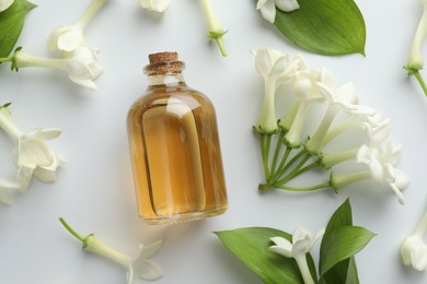 Photo of Bottle of essential oil, jasmine flowers and green leaves on white background, flat lay