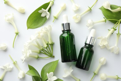 Photo of Bottles of essential oil, jasmine flowers and green leaves on white background, flat lay