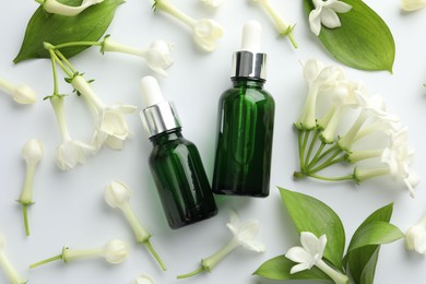 Photo of Bottles of essential oil, jasmine flowers and green leaves on white background, flat lay