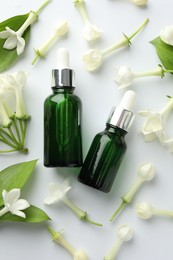 Photo of Bottles of essential oil, jasmine flowers and green leaves on white background, flat lay