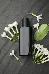 Photo of Perfume, jasmine flowers and green leaf on black table, flat lay