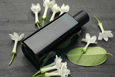 Photo of Perfume, jasmine flowers and green leaf on black table, closeup