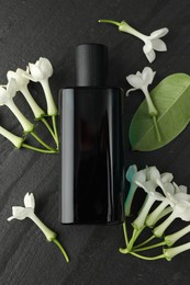 Photo of Perfume, jasmine flowers and green leaf on black table, flat lay