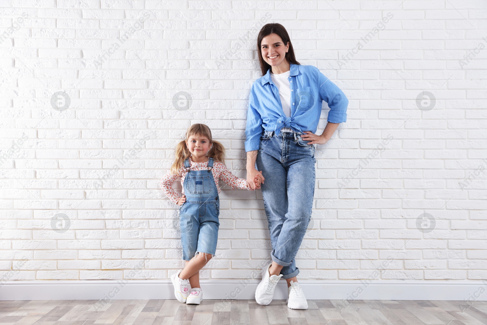Beautiful mother and her little daughter near white brick wall Photo of Beautiful mother and her little daughter near white brick wall